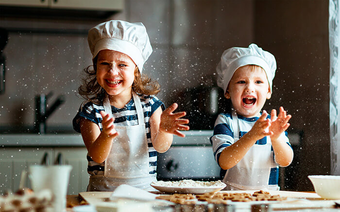 Niños con delantal de cocina jugando con harina en la cocina