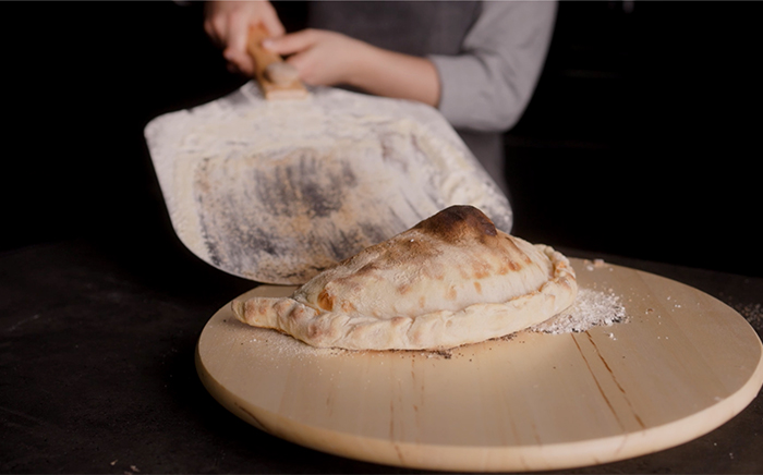 persona dejando un calzone con una pala de pizza sobre un plato de madera