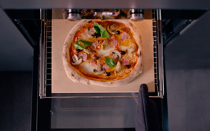 horno abierto con una pizza sobre una piedra en la rejilla sujetada por una mano