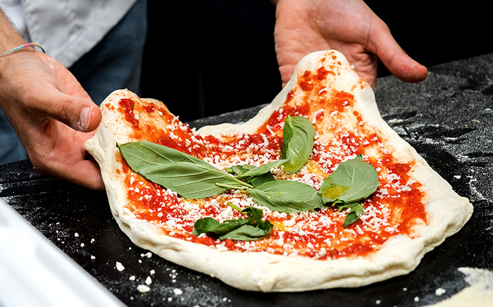 pizza sin hacer con tomate albahaca y queso sujetado por manos hombre