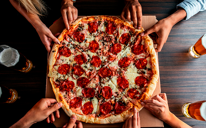 pizza sobre caja de cartón cortada en porciones y manos cogiéndolas