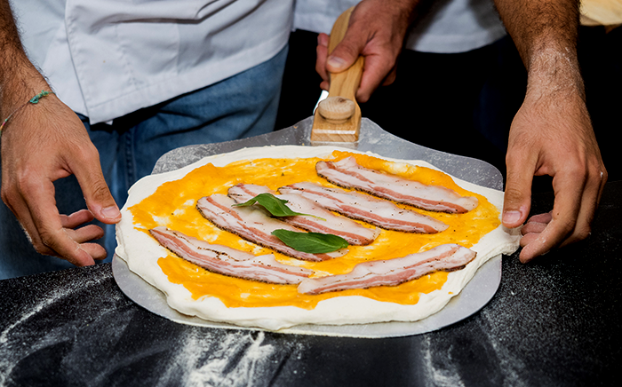 hombres sujetando pala de pizza con pizza de calabaza y panceta