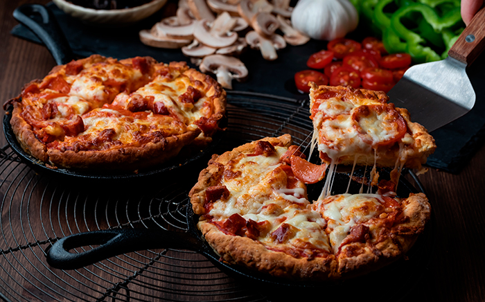 dos pizzas en sartén con una porción cortada y elevada con queso fundido