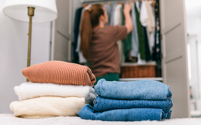 Ropa doblada en una cama con chica al fondo colocando ropa en un armario