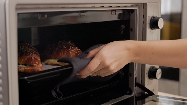 horno abierto y mujer metiendo una bandeja de croissants dentro