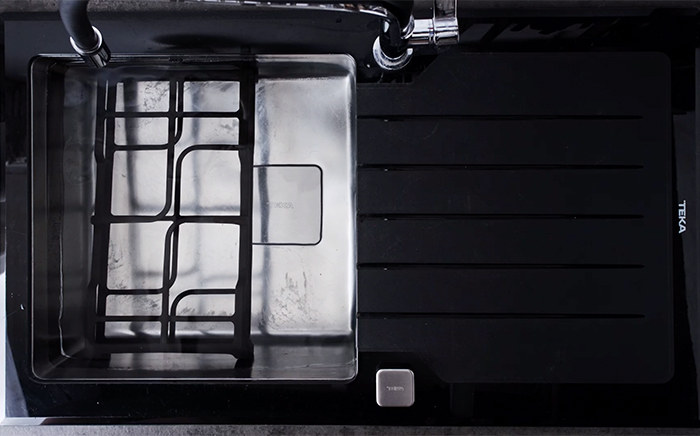 rejillas de una placa de gas sumergidas en agua en un fregadero de cristal negro teka