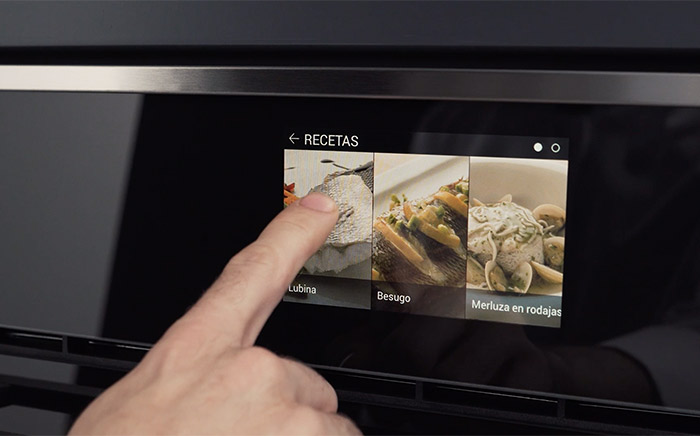 mano seleccionando en el display de un horno teka una receta de lubina al horno