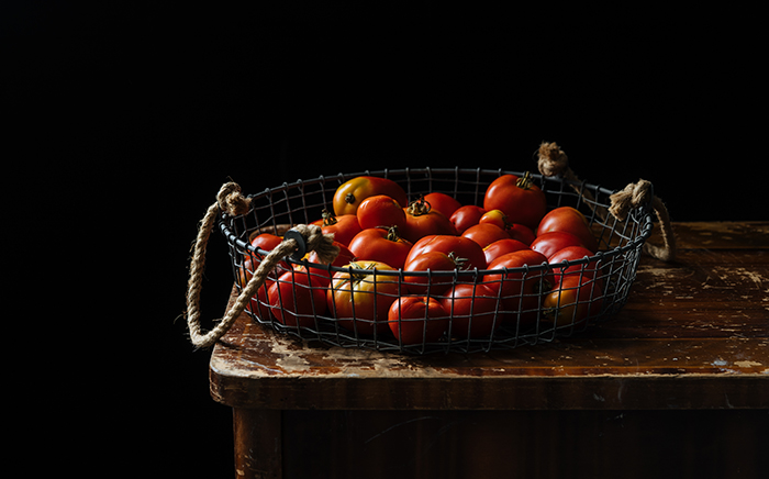 cesta de hierro con tomates dentro apoyada sobre una mesa de madera