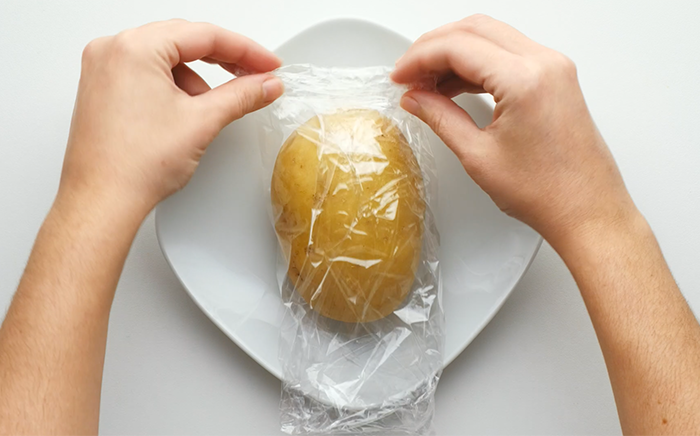 manos envolviendo una patata en papel film transparente