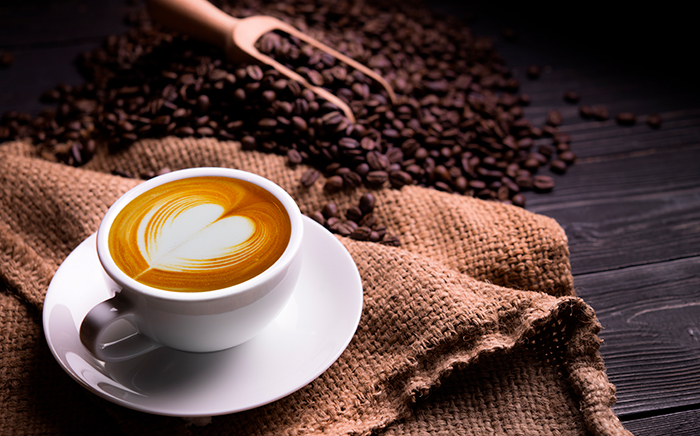 taza de café con espuma de leche y granos de café en una mesa