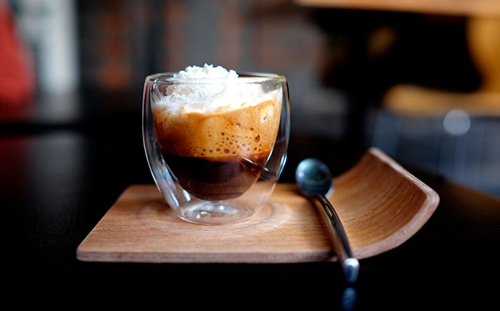 vaso de café con nata montada sobre una bandeja de madera y cucharita