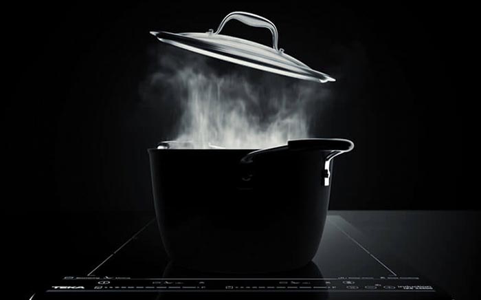 Olla en cocina Teka echando humo sobre fondo negro