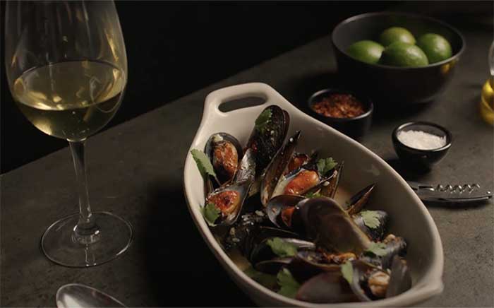 Copa de vino blanco con mejillones thai servidos en una fuente e horno blanca