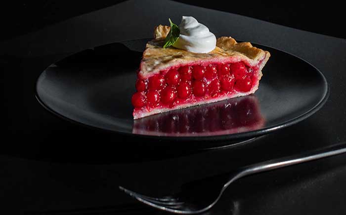 Pastel de grosellas con un poco de nata en un plato negro junto a un tenedor postre de San Valentín