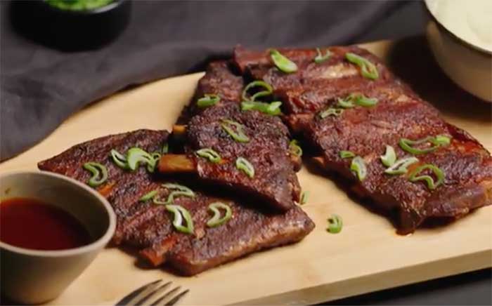 Costillas a baja temperatura servidas en una tabla de madera con salsas cocina al vapor sous-vide