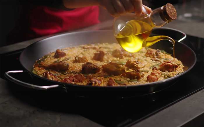 Mano echando un chorro de aceite sobre una paella cocinada con MestrePaeller de Teka