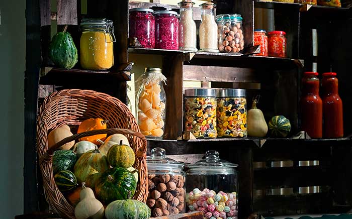 Despensa con tarros de cristal con alimentos organizados junto a cesta con verduras