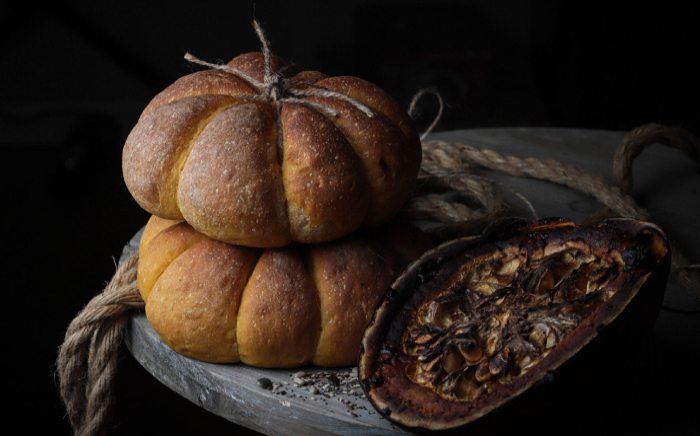 Calabazas y panes de calabaza en una encimera rústica sobre fondo negro para hablar de recetas de Halloween