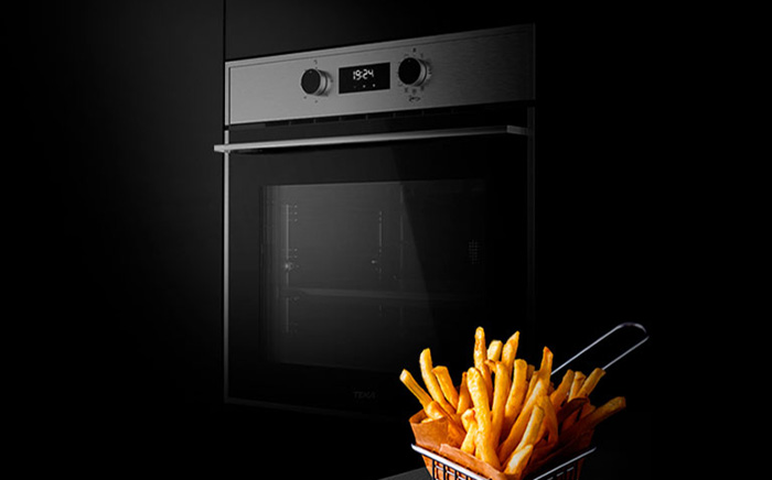 Horno AirFry de Teka en plano frontal con una cesta de metal con patatas fritas recién hechas en primer plano