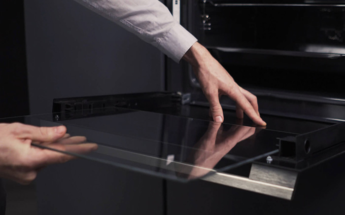 Dos manos retirando los cristales de la puerta de un horno para su limpieza