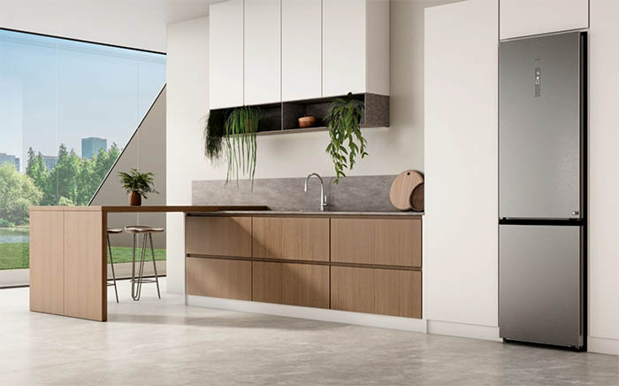 Cocina de diseño abierta y amplia con muebles en madera, un frigorífico energéticamente eficiente de Teka de segunda generación y un ventanal mostrando un jardín al fondo