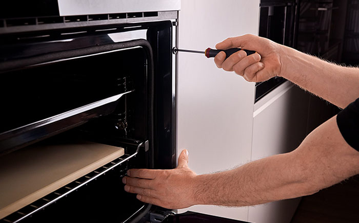 Servicio técnico de Teka arreglando las averías de horno más comunes, con unos brazos atornillando un horno a su base definitiva