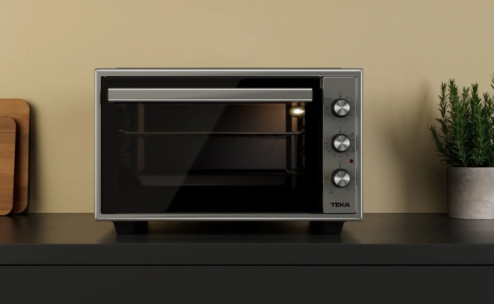 Horno sobreencimera GrandChef de Teka entre unas tablas de madera de cortar y una planta en un tiesto de hojalata como ejemplo de electrodomésticos para cocinas pequeñas