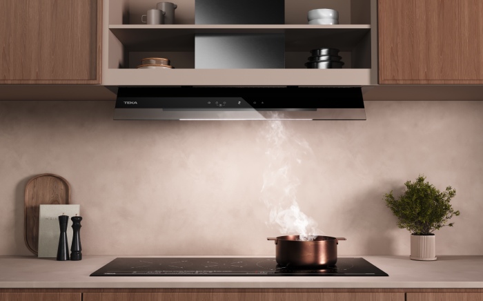 Plano medio de una cocina de inducción negra con una olla color cobre cocinando en la que el vapor desaparece por la campana Integra Pro de Teka situada justo encima, totalmente integrada e invisible, con espacio para almacenaje