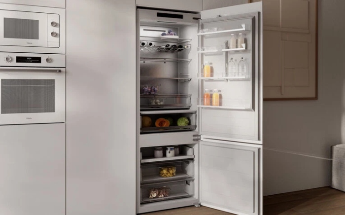 Frigorífico encastrable de Teka con la puerta abierta en una cocina blanca con horno y microondas en columna a la izquierda