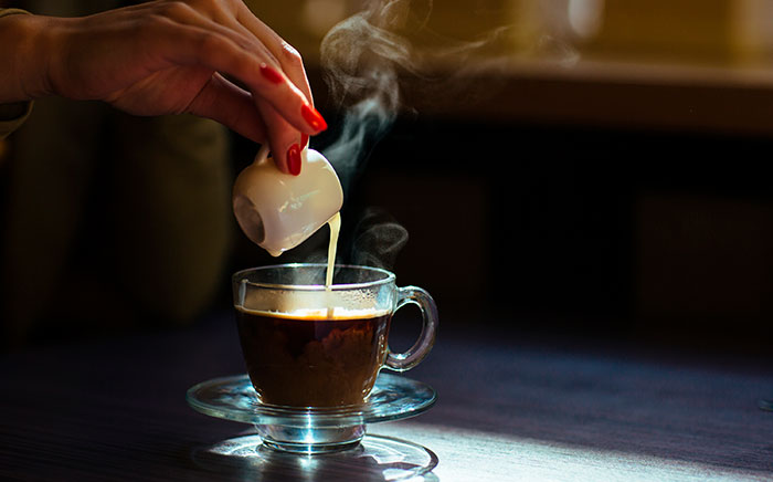 A hand pouring milk in a crystal cup to prepare a macchiato