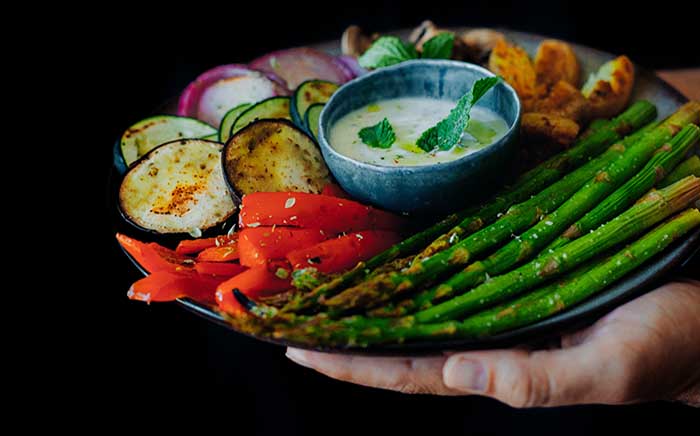 grilled vegetables served on a plate by a couple of hands and including sauce in the middle