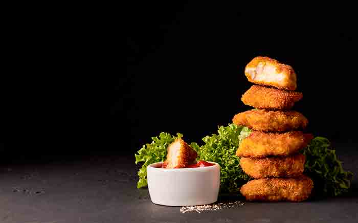 Crispy nuggets one over the other with a bowl of sauce on a black background