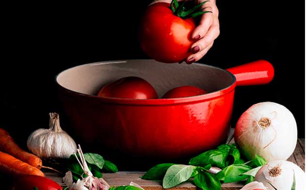 Tomatos, onion, basil, carrots and other vegetables in a red saucepan