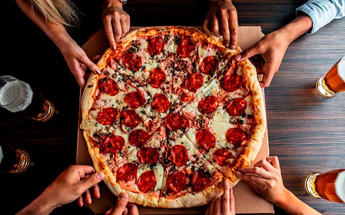 Pepperoni pizza with several hands around ready to grab a pizza slice