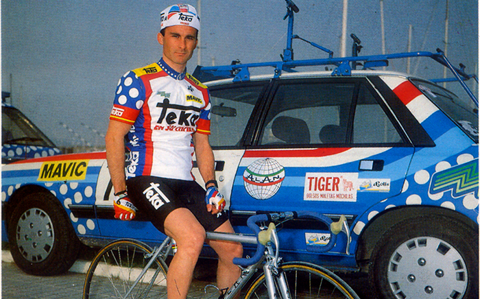 Teka's cyclist in his bicycle with a vehicle from the race on the background