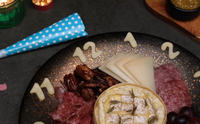 A platter of appetizers with cold cuts, cheese and other recipes with the shape of a clock on a dark Christmas surface
and celebration items