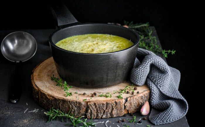 Warm, courgette soup as comfort food for a Blue Monday arranged over a tree stub with cooking herbs around and a grey tea towel