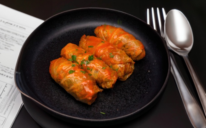 Steamed stuffed cabbage arranged on a black plate with a fork and a spoon on the right side and work paper on the left