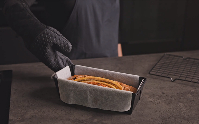 A hand holding a sponge cake inside a rectangular, metal mould, over a working surface