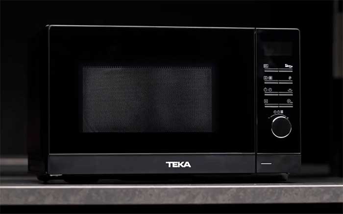 Black Teka microwave oven with control panel on the side, sitting on a working surface.
