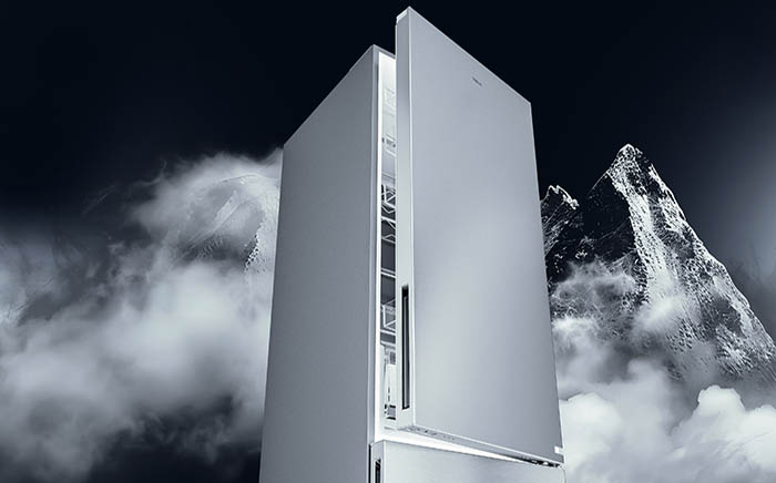 Teka fridge freezer with door open revealing interior shelving, set against a moody black and white mountain landscape