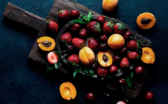 Assorted summer fruit on a dark working surface