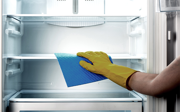 A hand in glove cleaning the empty shelves of an open fridge freezer