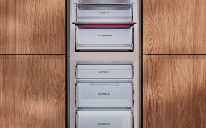 Close-up of stacked internal drawers including Cooling Box, VitaCare Box, and Freezer Box compartments inside a built-in refrigerator framed by wood cabinetry.