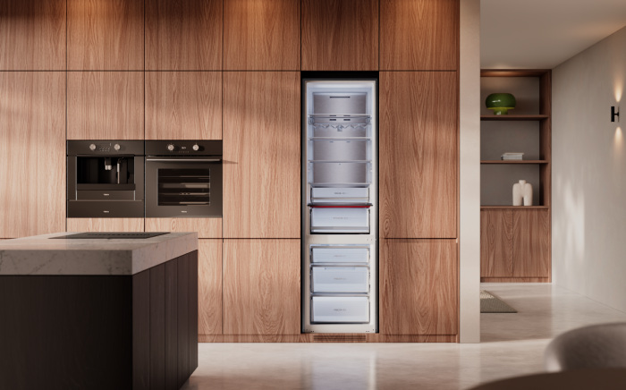 Open built-in refrigerator Teka's Built-in Max integrated into warm wood kitchen cabinetry alongside built-in ovens and a marble kitchen island.