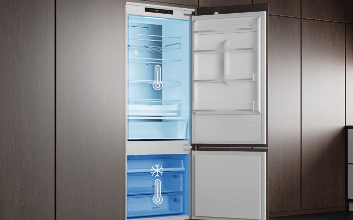 Open In-Line, slot-in Teka's refrigerator and freezer with blue-glowing interior compartments, featuring a thermometer icon in the fridge and a snowflake with a thermometer icon in the freezer to indicate temperature control.