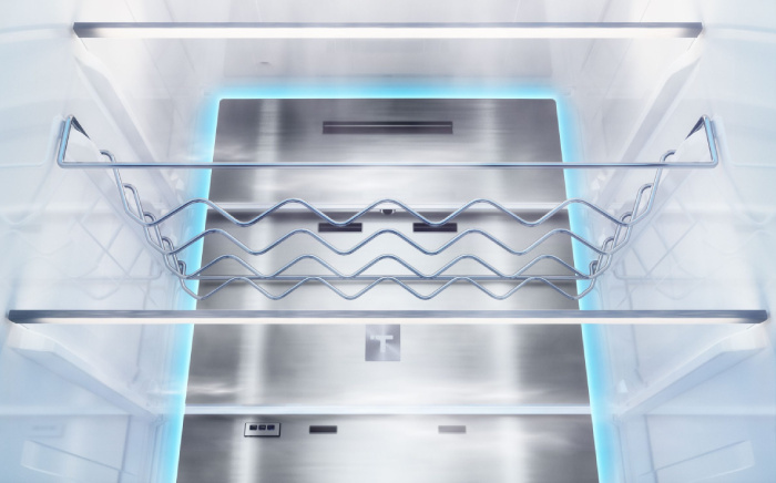 Close-up of a stainless steel metal cooling back panel inside an empty refrigerator, featuring LED lighting and a chrome wine rack.