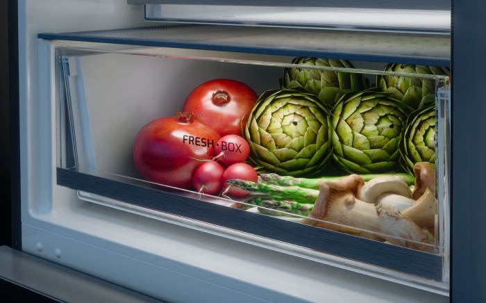 Refrigerator crisper drawer, FreshBox by Teka, filled with fresh produce including pomegranates, artichokes, and asparagus.