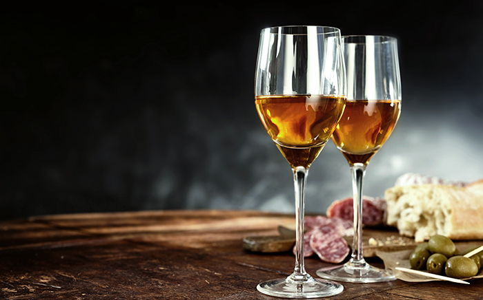 Two glases of sherry wine with deli meats, bread and olives over a black background