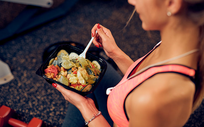 A woman in a aerobic outfit is ready to eat a sort of healthy and yummy salad from a food container